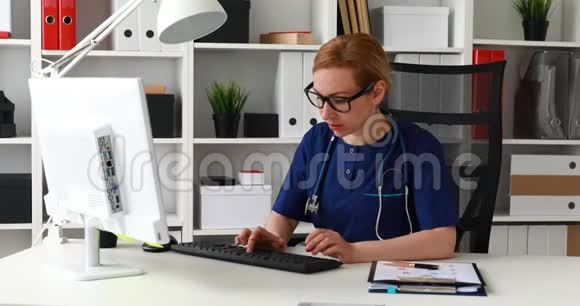 穿蓝色实验室外套的医生坐在工作场所在电脑上工作视频的预览图