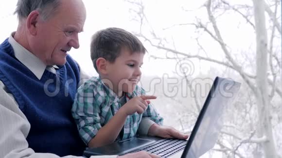 回家的时候孙子孙女带着爷爷在窗后的笔记本上看动画片视频的预览图