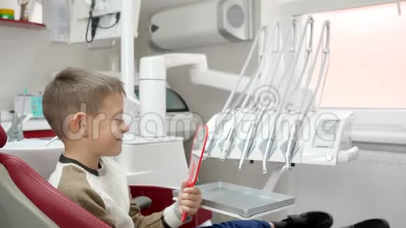 快乐的孩子坐在牙科椅上在现代设备的背景下照镜子视频的预览图