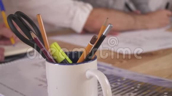 一个拿着剪刀和记号笔的铅笔的杯子在背景中一群办公室工作人员在画画视频的预览图