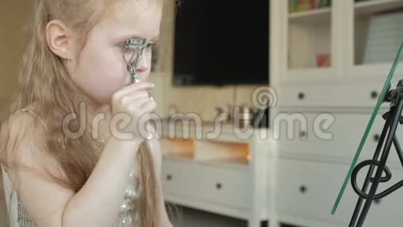 头发红的小女孩试图用钳子卷睫毛照镜子化妆脸时尚风格视频的预览图