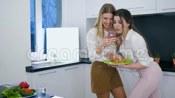 快乐的女朋友们白天吃早午饭时在厨房拿着手机视频的预览图