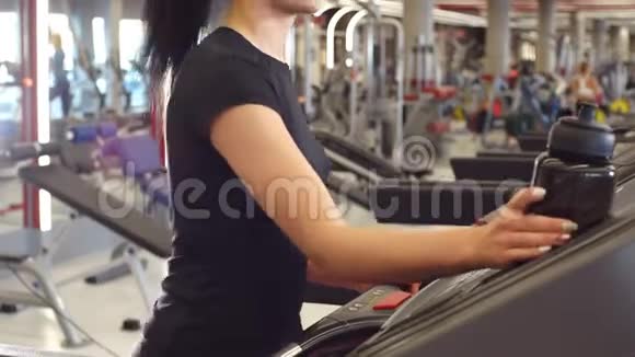 年轻女孩带着摇瓶水在跑步机上行走视频的预览图