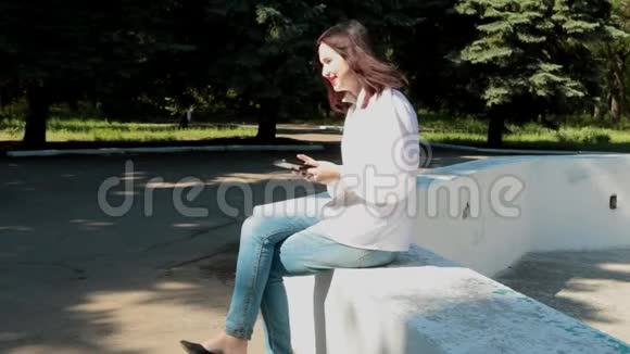 女孩坐在公园的喷泉上玩游戏视频的预览图