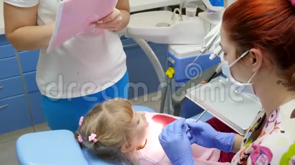 戴医用口罩的女医生使用工具治疗小病人及助手旁的牙齿视频的预览图