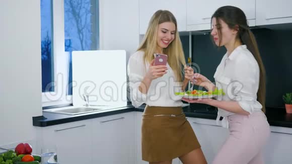 有用的食物快乐的女朋友在厨房午餐时在android上看照片视频的预览图