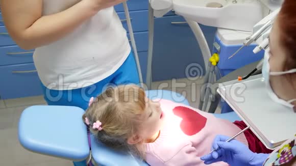 小女孩躺在牙科椅上与口腔医生协商在诊所里拿着工具视频的预览图