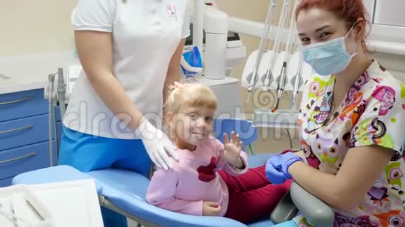 戴着橡胶手套戴着医用口罩坐在牙齿矫正器旁边的扶手椅上一位漂亮的病人挥舞着手视频的预览图