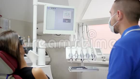 戴医用口罩的男医生负责女性病人口腔诊断并看电脑显示器视频的预览图