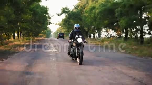 阳光明媚的一天一名身穿灰色头盔皮夹克和格子衬衫的男子骑摩托车在柏油路上视频的预览图