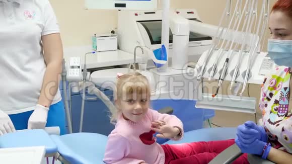 坐在牙科椅上时可爱的孩子挥舞着手旁边是戴着橡胶手套和医用口罩的医生视频的预览图