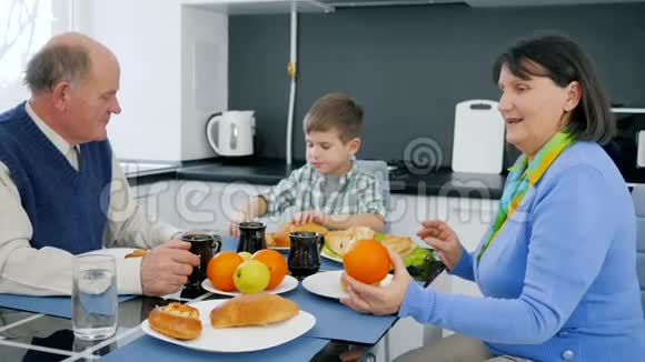 奶奶和爷爷用美味的面包制品和茶和水果喂小男孩视频的预览图