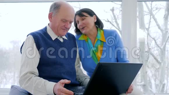 在线支付现代老人幸福的夫妻在家里用电脑在Skype交谈视频的预览图