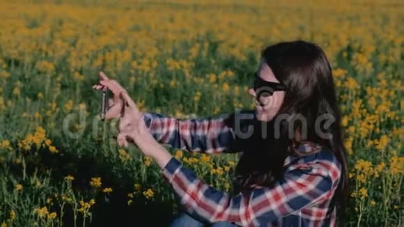 女人在手机上自拍坐在黄花间的草地上视频的预览图