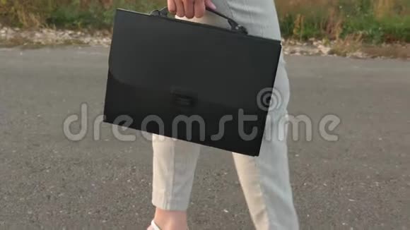 女商人手里拿着黑色公文包穿着裤子和夹克的女人走在沥青路上侧视着视频的预览图