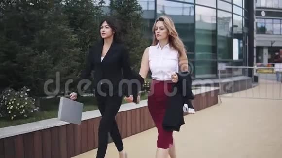 穿商务西装的女孩和一个穿裙子和衬衫的同事一起来商业妇女在街上与视频的预览图