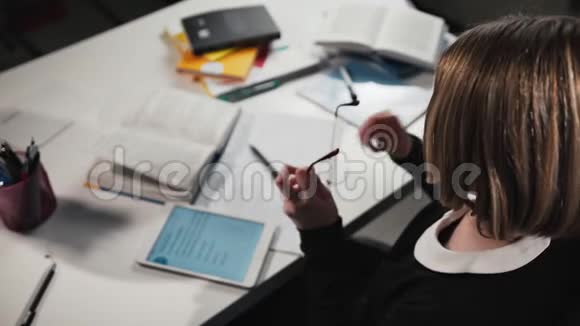女生或学生擦眼镜的特写使用平板电脑并在工作簿中书写她在做作业视频的预览图
