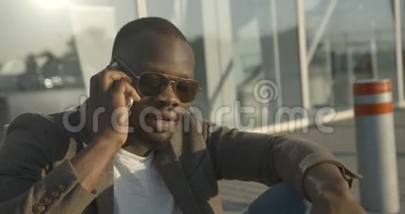这位英俊时尚的非洲男人戴着太阳镜通过手机进行情感交谈并制作了一幅特写肖像画视频的预览图