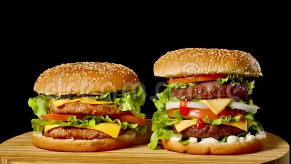 特写两个开胃汉堡与芝麻包子旋转的黑色背景快餐无缝循环镜头视频的预览图