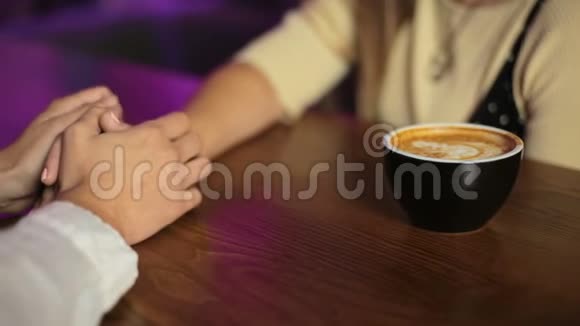 年轻一对情侣正坐在咖啡馆里喝着咖啡开心地笑着双手合拢视频的预览图