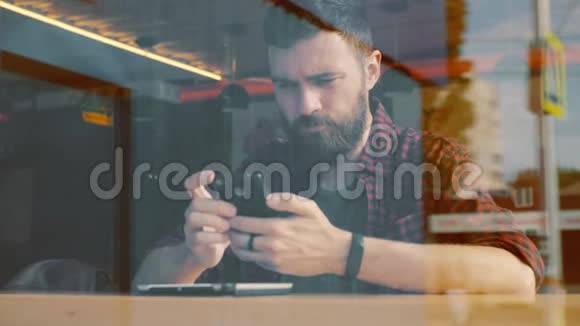 在咖啡馆的智能手机上使用应用程序的人从窗户射中视频的预览图