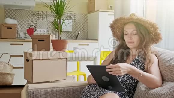 女人用平板电脑后面有盒子新房子里带手机的年轻美女画像视频的预览图