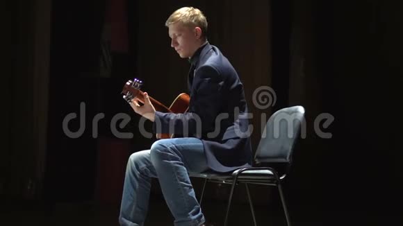 男子在舞台上演奏声吉他在聚光灯下拔掉插头的表演侧视视频的预览图
