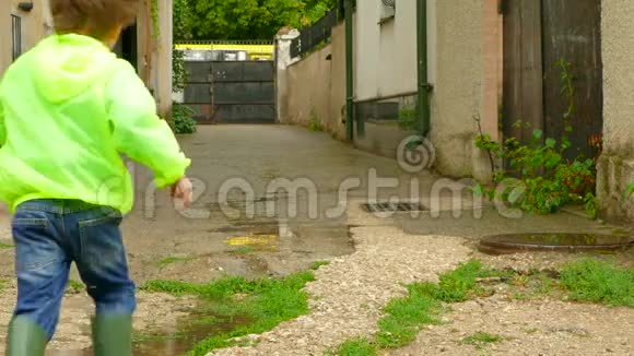 穿着雨衣的男孩穿着橡胶靴在院子里跑来跑去视频的预览图