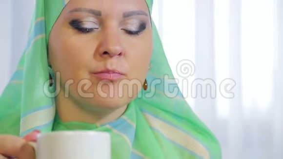 一个身穿浅色围巾的年轻穆斯林妇女在咖啡馆里吃蛋糕喝茶视频的预览图