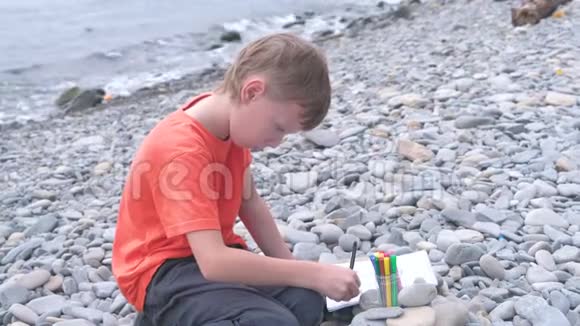 男孩坐在海边的石滩上画着记号视频的预览图