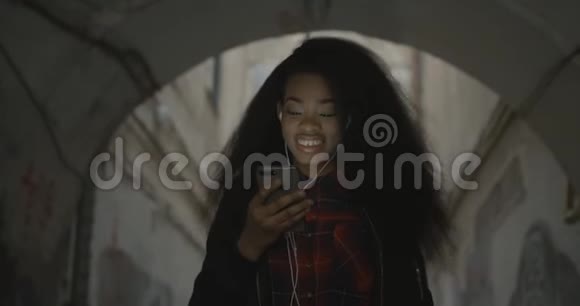 微笑的美丽的非洲女孩在户外听音乐时通过手机跳舞和发短信的肖像4k视频的预览图
