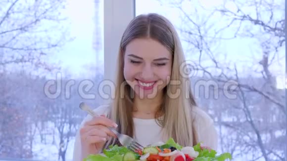 漂亮的女孩在家里大窗户的背景下吃蔬菜沙拉视频的预览图