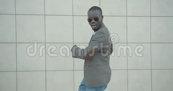 滑稽的微笑英俊的非洲男人穿着时髦的衣服戴着太阳镜在后台散步时跳舞视频的预览图