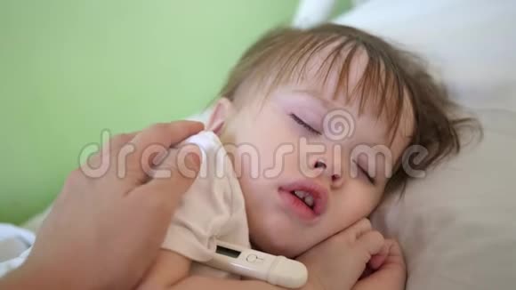 妈妈用温度计测量婴儿的体温用手抚摸孩子特写镜头婴儿睡在医院病房视频的预览图