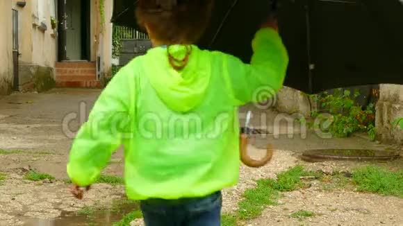 穿着橡胶靴的男孩带着雨伞在院子里跑来跑去视频的预览图