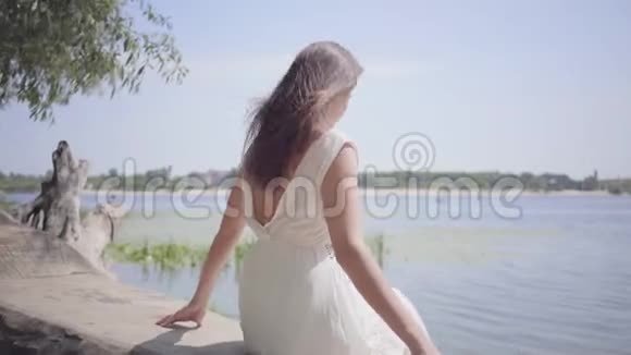 肖像迷人的年轻女孩留着长长的黑发穿着白色的夏装坐在上面视频的预览图