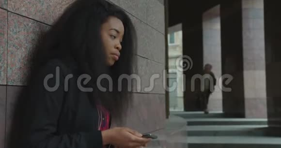 侧写年轻美丽迷人的非洲女孩听音乐耳机发短信聊天移动户外4k独自视频的预览图