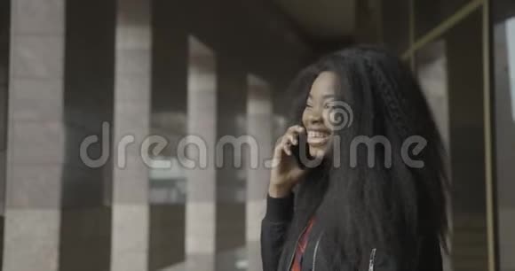 快乐的微笑漂亮的年轻非洲女孩通过手机说话笑室外位置4K录像视频的预览图