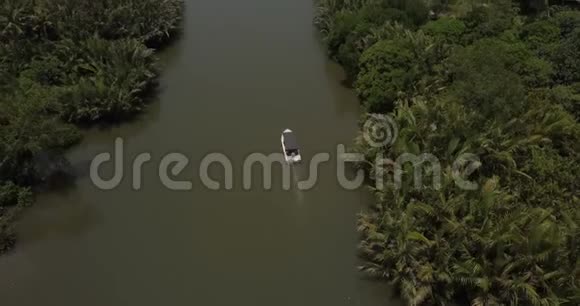 在荒野中一艘白色的狩猎小船远离无人机摄像机沿着平静的丛林河航行视频的预览图