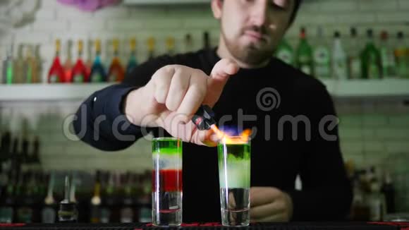 酒吧表演手臂较轻的家伙点燃鸡尾酒酒吧柜台上薄薄的玻璃中的彩色层视频的预览图