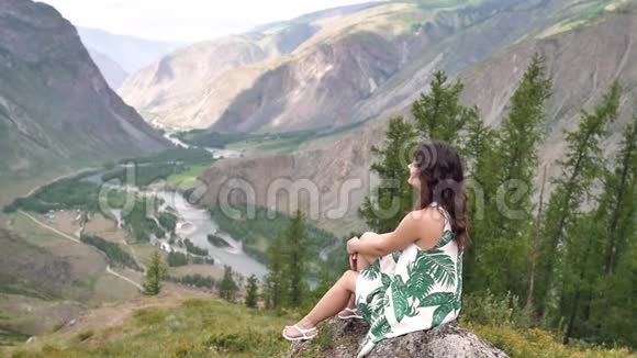 一个年轻的女人坐在山上穿着一件漂亮的衣服享受大自然视频的预览图