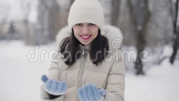 布鲁奈特的头发是年轻女性她的嘴唇是粉红色的穿着米色羽绒大衣戴着帽子远离镜头在雪域中央调情视频的预览图