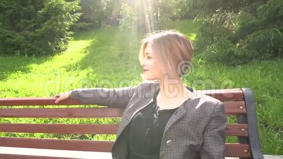 相机远离美丽的时尚年轻女子坐在阳光下的夏日公园的长凳上视频的预览图