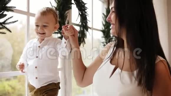 年轻的母亲正牵着儿子手而他正走在装饰着圣诞花环的窗台上快乐视频的预览图