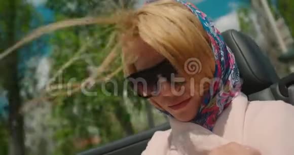 微笑美丽的女人与自然化妆正在享受旅行在敞篷车她戴着太阳镜和围巾视频的预览图