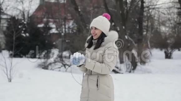 布吕内特的头发是年轻女性她的嘴唇是粉红色的穿着米色羽绒大衣戴着帽子享受着下雪的中央公园视频的预览图