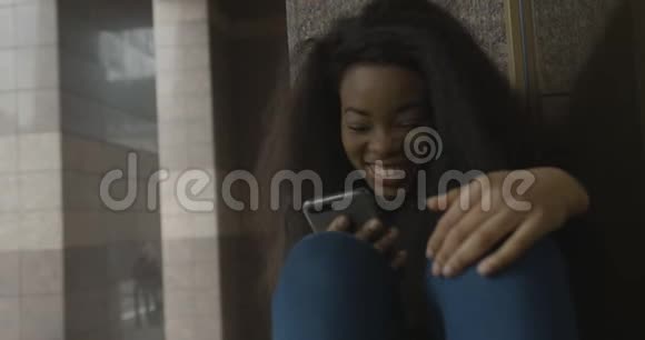 嘲笑漂亮的非洲女孩漂亮的女士坐在楼梯上通过手机聊天和浏览4k视频的预览图