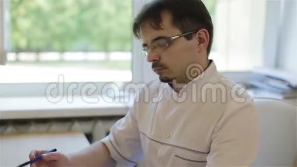 戴眼镜的医生坐在一张桌子上在文件里写字视频的预览图