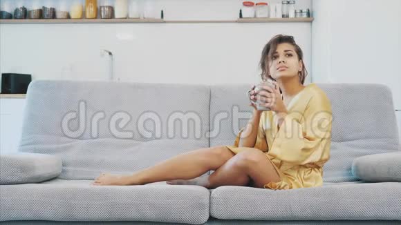 穿着浴袍的年轻女子坐在沙发上的房间里他坐在沙发上喝咖啡看电视舒适视频的预览图