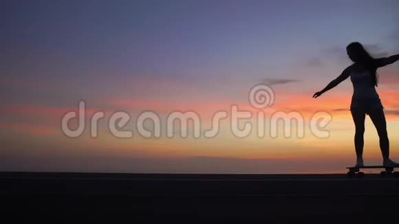 美丽的女孩骑着滑板在夕阳的天空下上路视频的预览图